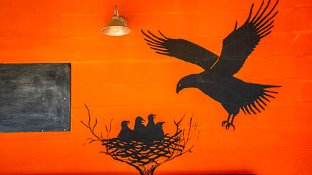 Simple but vivid unsigned mural on one of the community support buildings along Graham Street, near the Karrawa Wirinya Coffee spot, which is part of the Birdsville Community Centre precinct. The use of black silhouettes on a bright ochre background evokes both the desert palette and traditional storytelling through shadow and form. [1047]