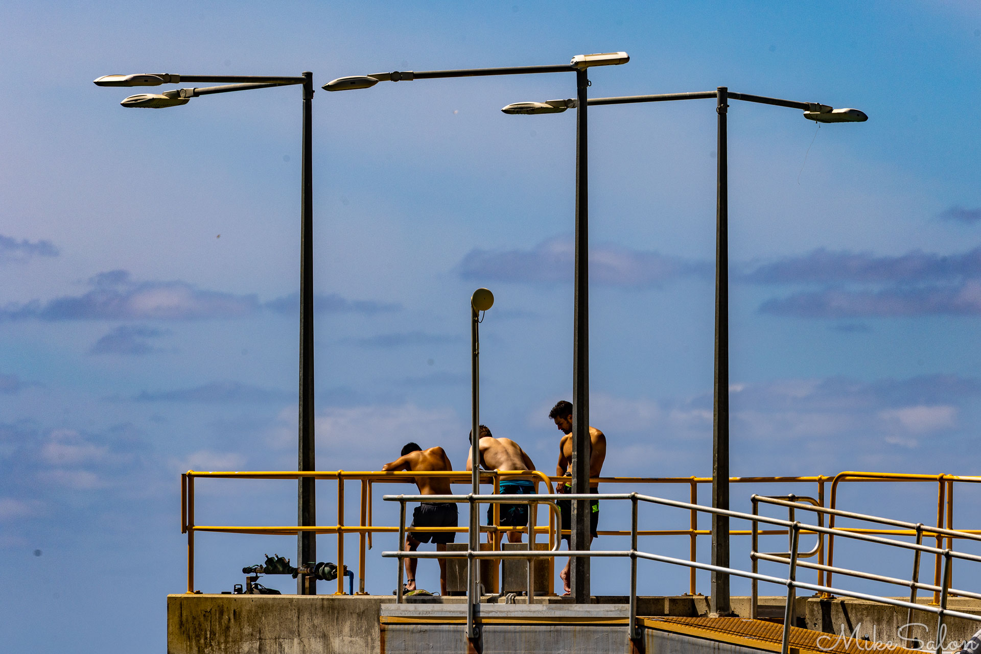 Shirtless youths watching activities at the end of a jetty. [9859]