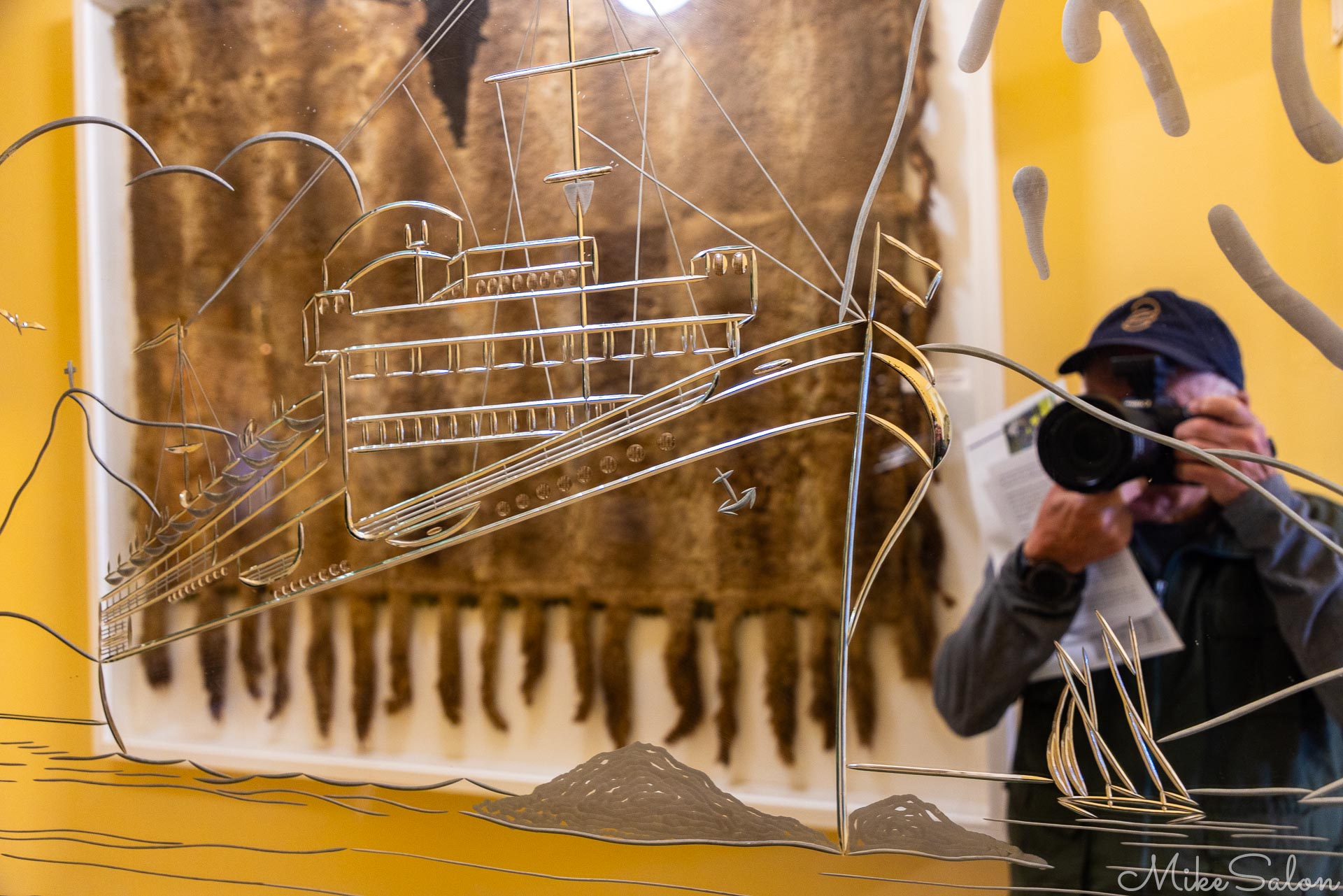 Reflection of photographer in a mirror embossed with outline of a large cruise liner. [5098]