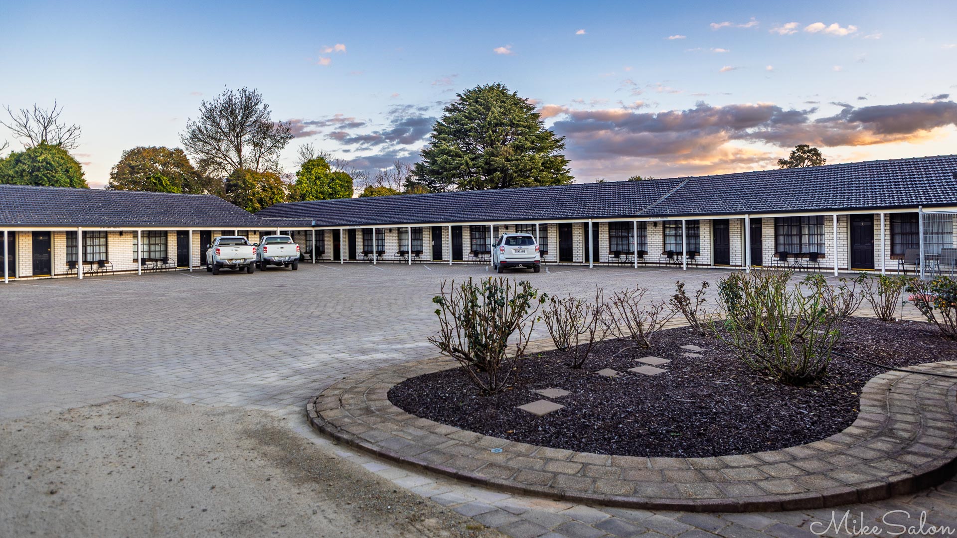 Bare and bleak motel forecourt with three vehicles. [5102]