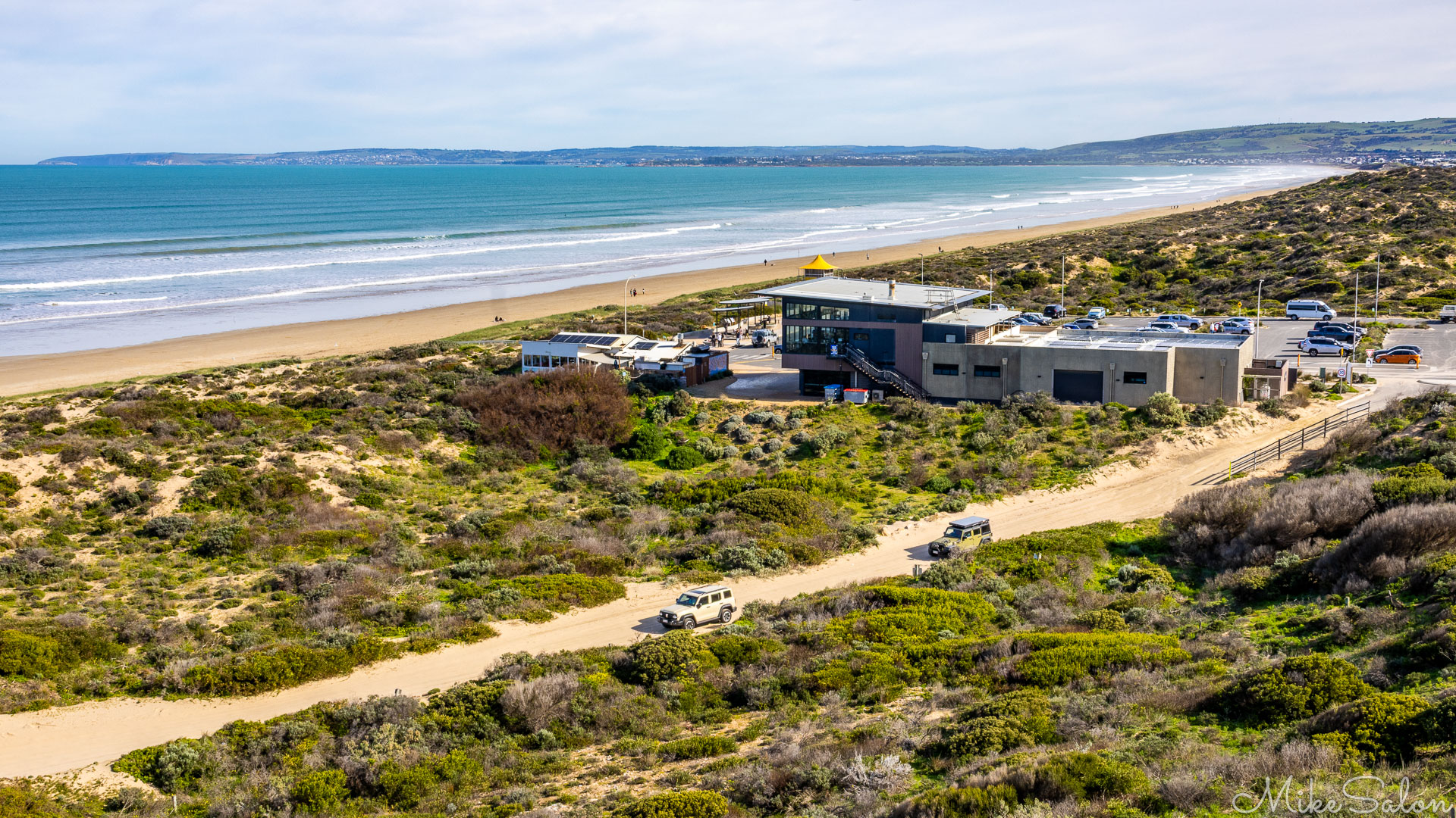From the whale watching boardwalk, Goolwa Beach looking west showing the surfclub, parking lot, and 4WD track to the beach. [2027]