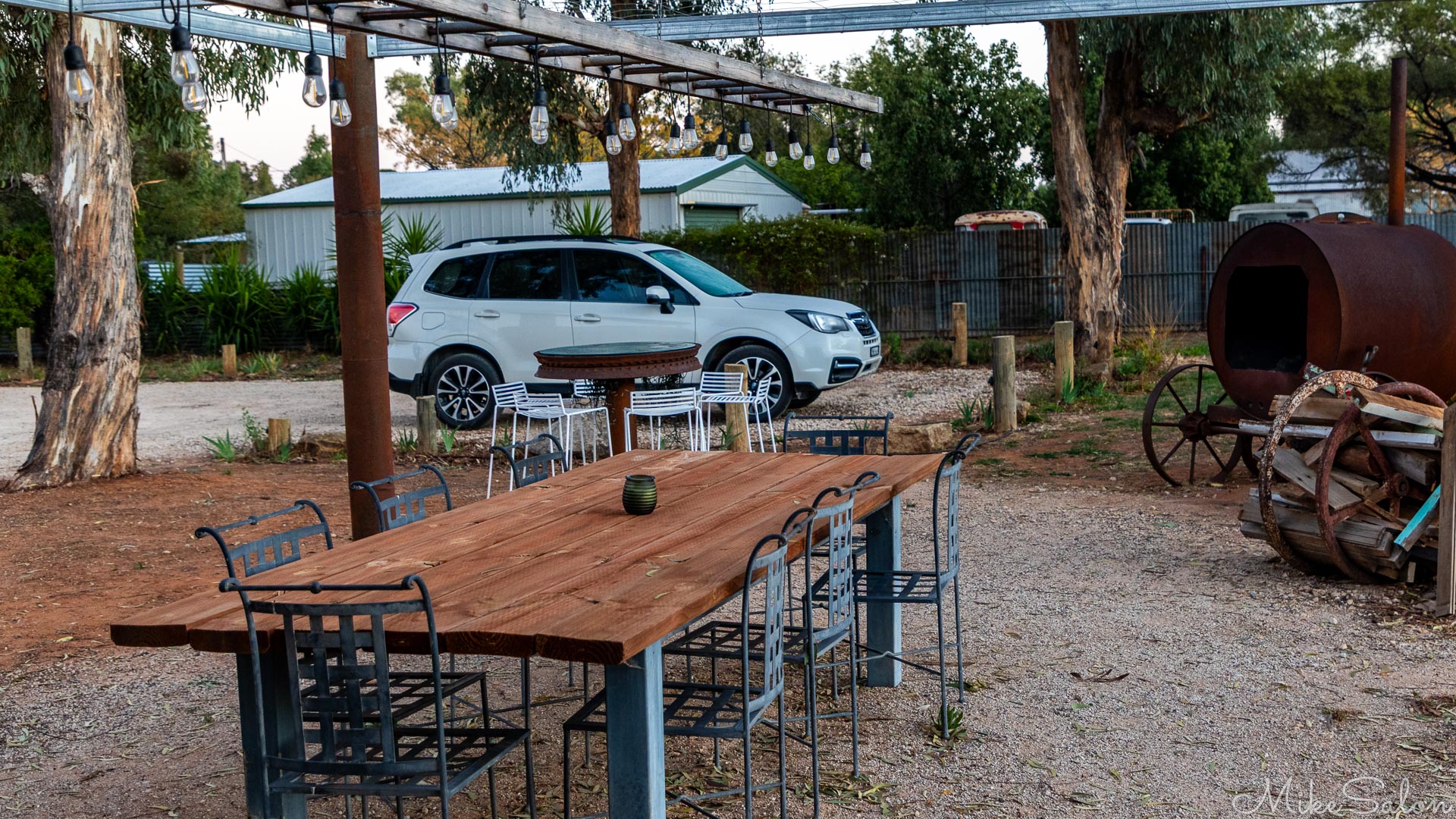 Accommodation courtyard showing table and chairs, a firepit, and a parked car. [2020]