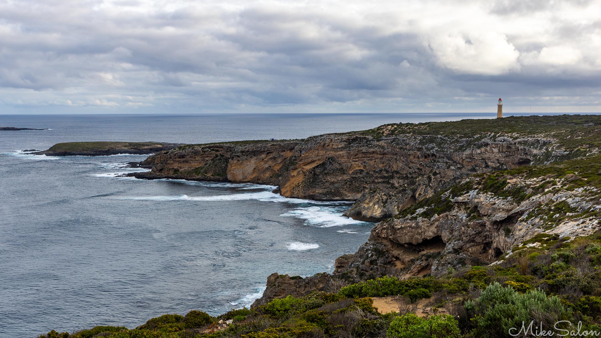 A cove and a distant lighthouse under threatening skies. [3735]