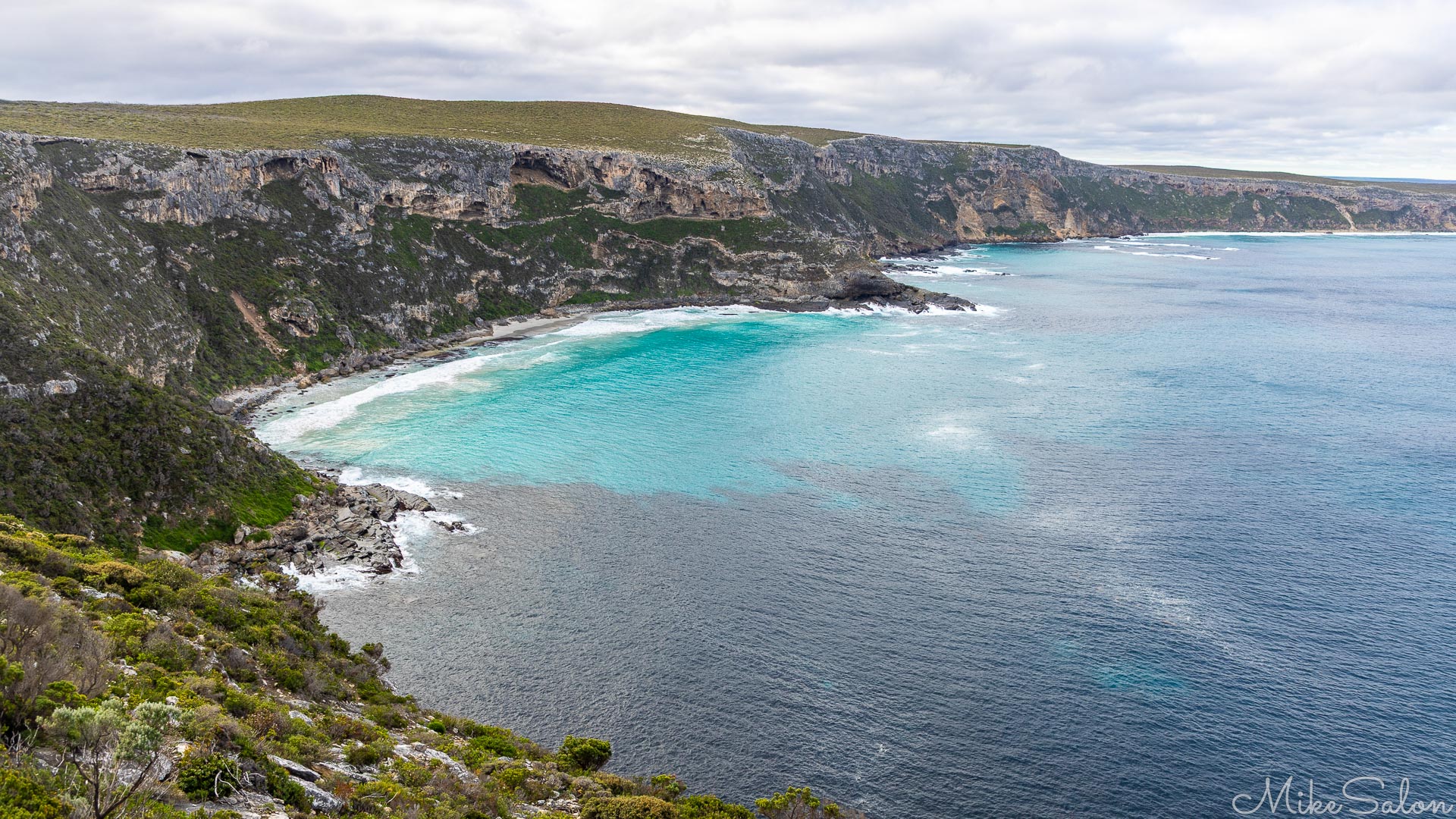 Steep cliffs leading down to a beach with crystal clear waters. [3729]