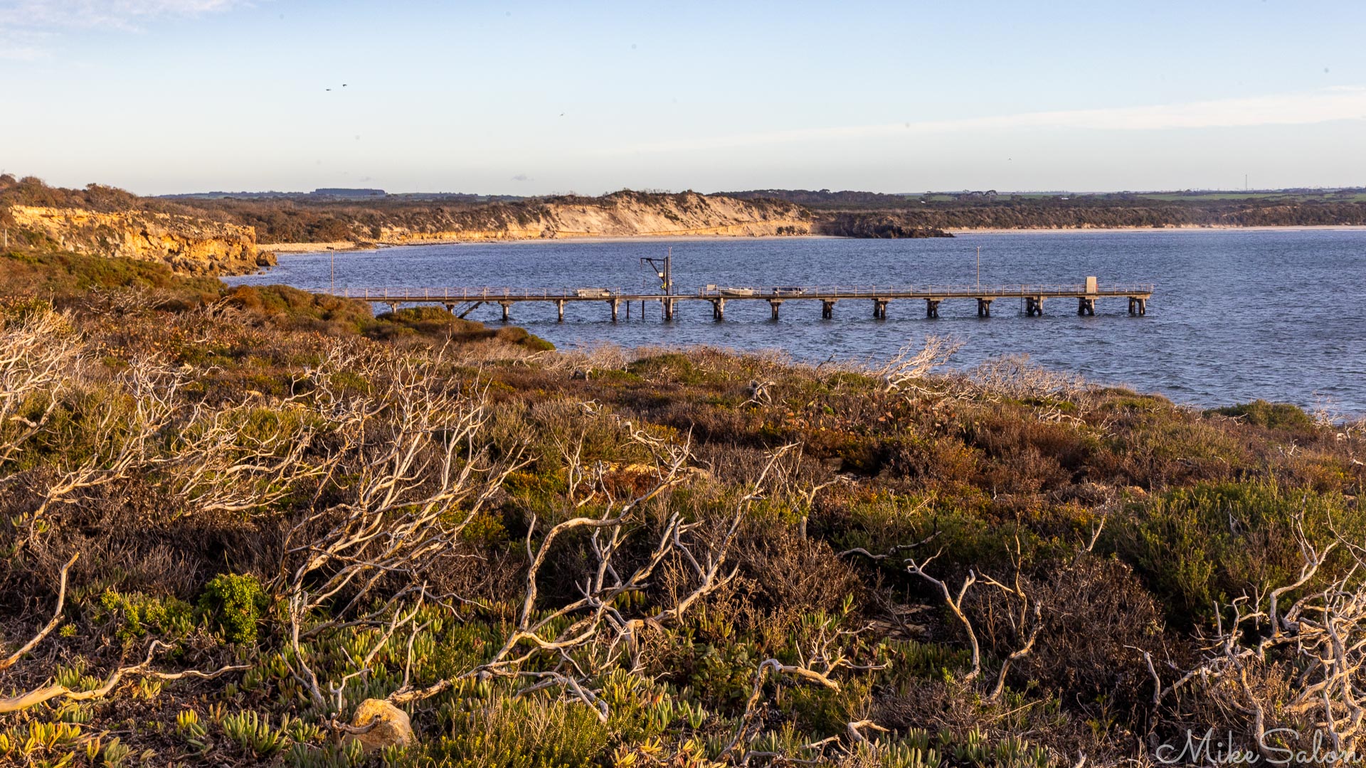 Across weathered heathland, an old jetty in a bay. [3857]