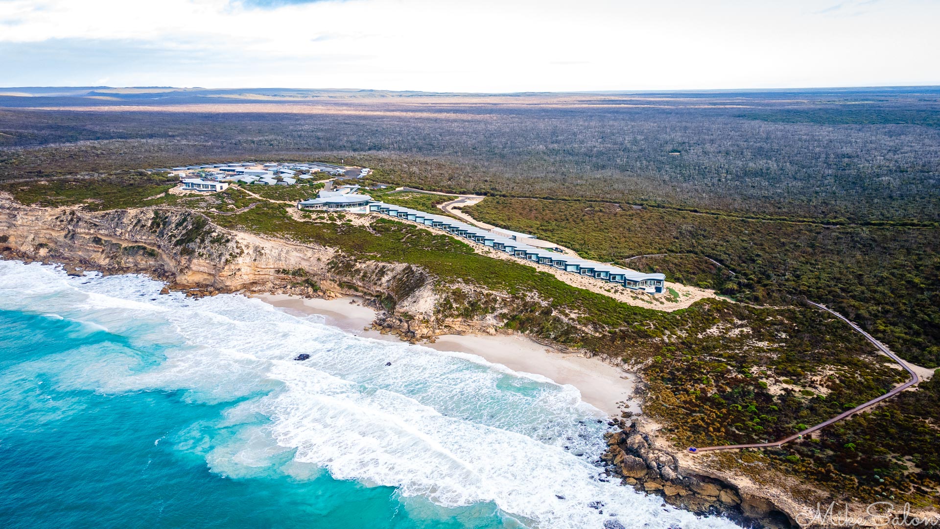Aerial view of an elongated lodge on a cliff overlooking a rough beach. [0988]
