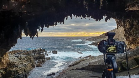 A camera set up ready under a huge arch and looking towards a rough sea inlet. [0208]