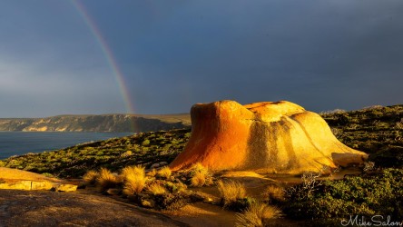 A colourful rock seen in dawn's first rays, with a rainbow and beach in the background. [4123]