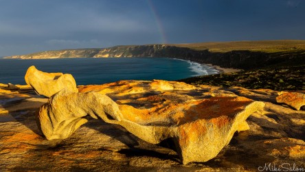 An irregular rock formation at dawn, with a beach and cape in the background. [4118]