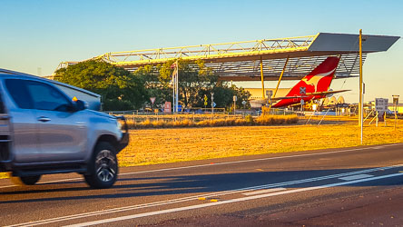 Traffic on Longreach`s Ilfracombe Road roars past the Qantas Founders Museum, the tail of a B-747 testing the height of the airpark roof. [2513]