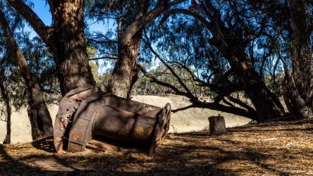 Rusted metal tank lying beneath trees.