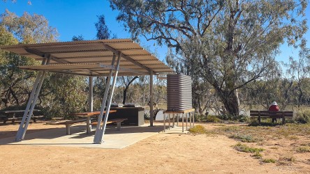 Metal‑roofed picnic shelter with benches in dry open area.