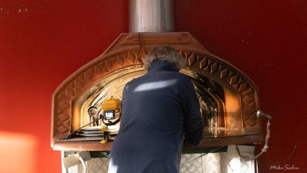 Cook tending a pizza oven inside a red‑walled kitchen.