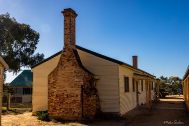Cream‑coloured house with stone chimney and tin roof.