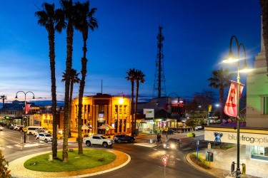City street with palm trees and buildings illuminated at dusk.