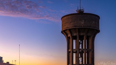Tall cylindrical water tower against colourful evening sky.