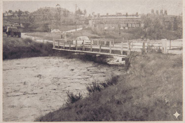 Cleaned up by AI, this very dirty photo on an interpretative plaque shows the now-gone wooden Bell Street bridge Mike used to cross on the way to school. Muscle Creek looks to be in flood. [5571]