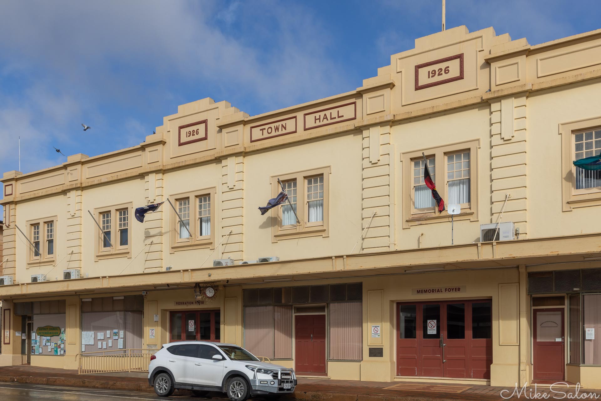 Cream‑coloured town hall with decorative façade and parked car in front.
