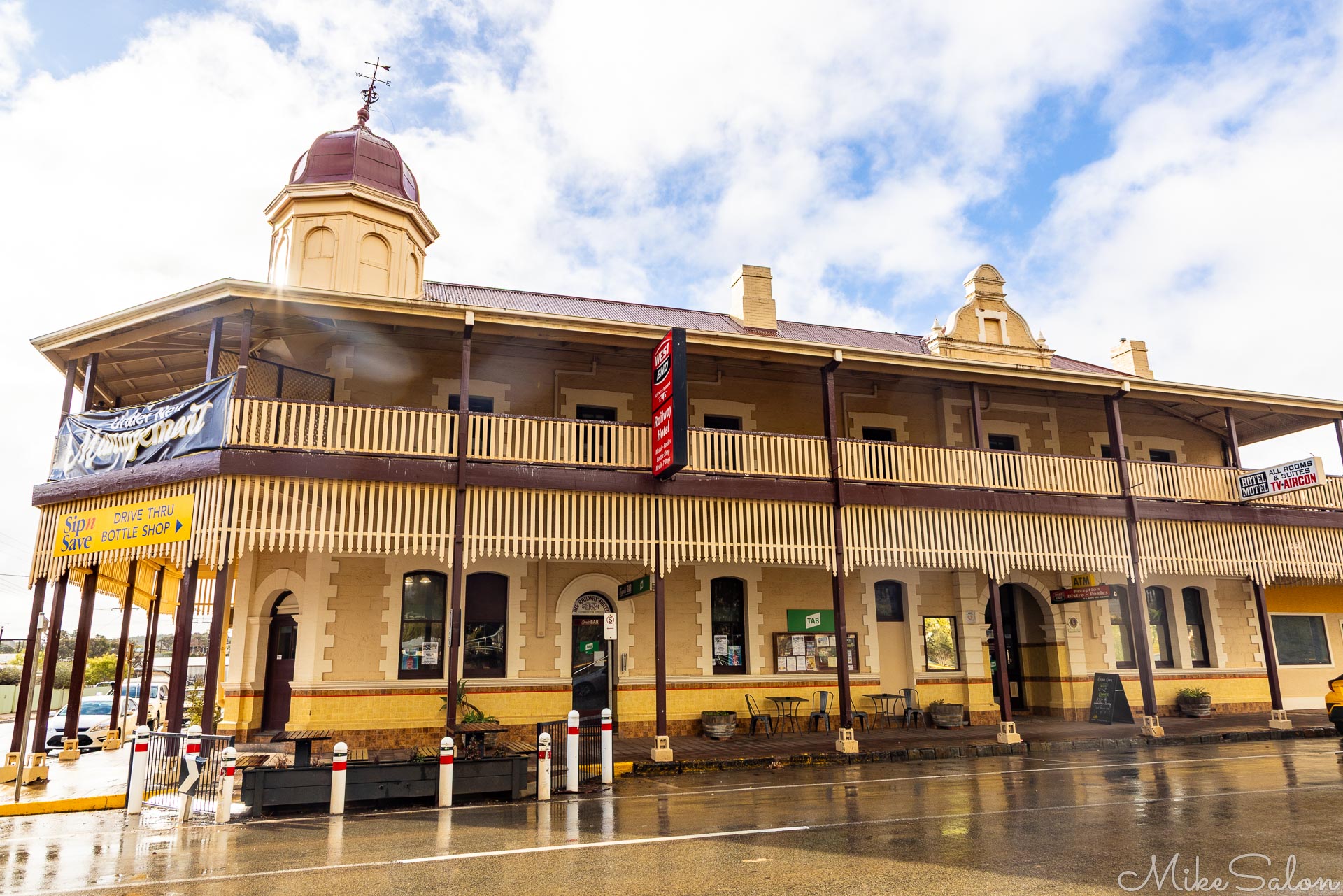 Large historic hotel with balcony and ornate roofline, wet street in foreground.