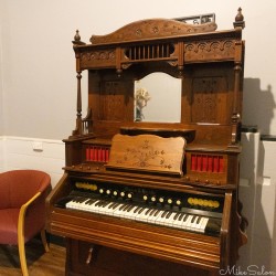 Ornate wooden player piano with carved details and music roll mechanism indoors.