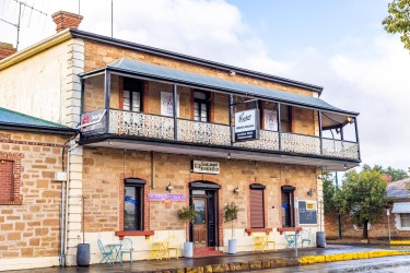 Two‑storey stone hotel with balcony and red trim on corner street.