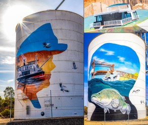Two tall silos with colourful murals depicting river scenes, fish, and boats under blue sky.