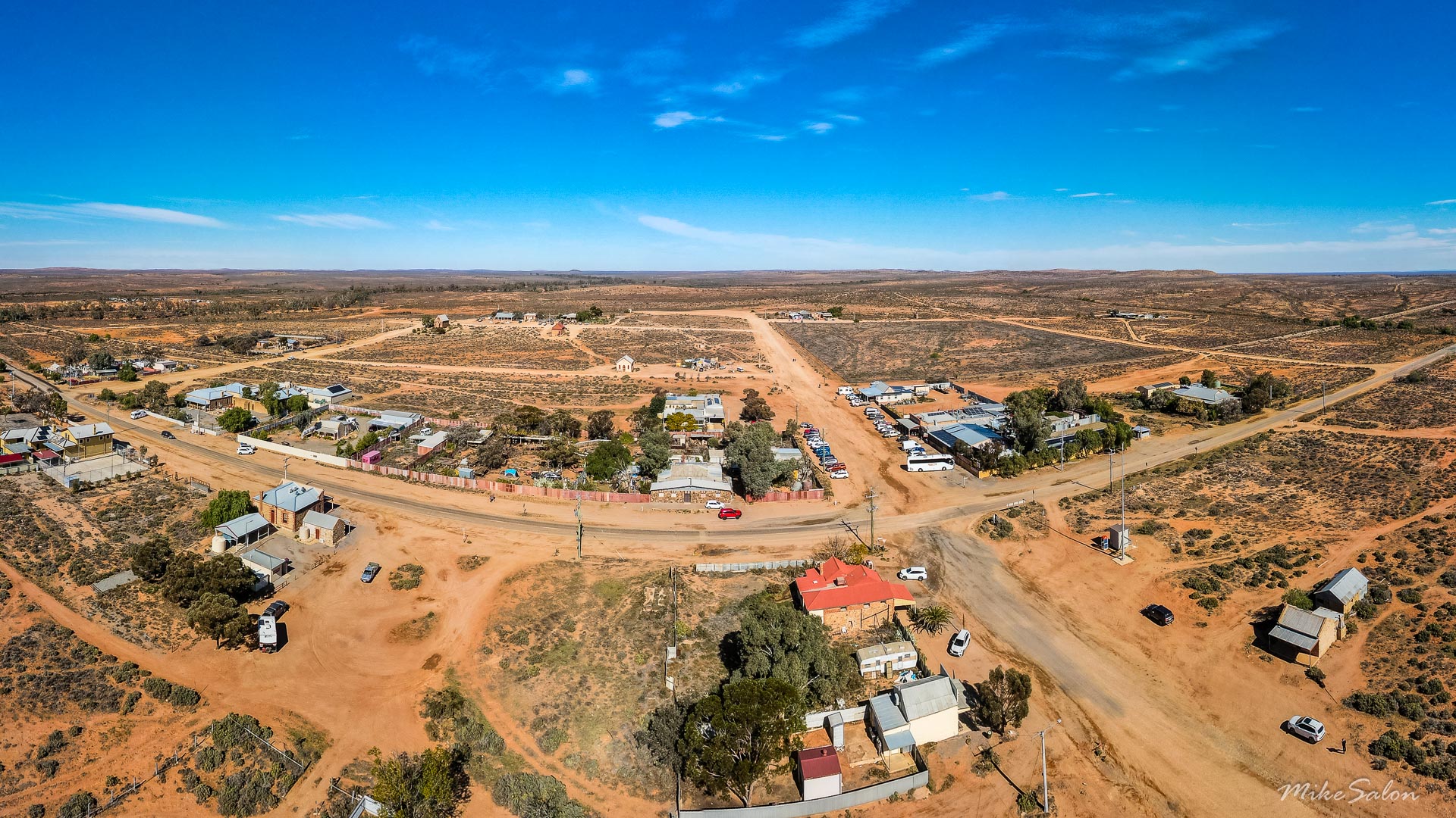 Aerial view of Silverton showing dirt roads, small buildings, and surrounding desert under clear blue sky.