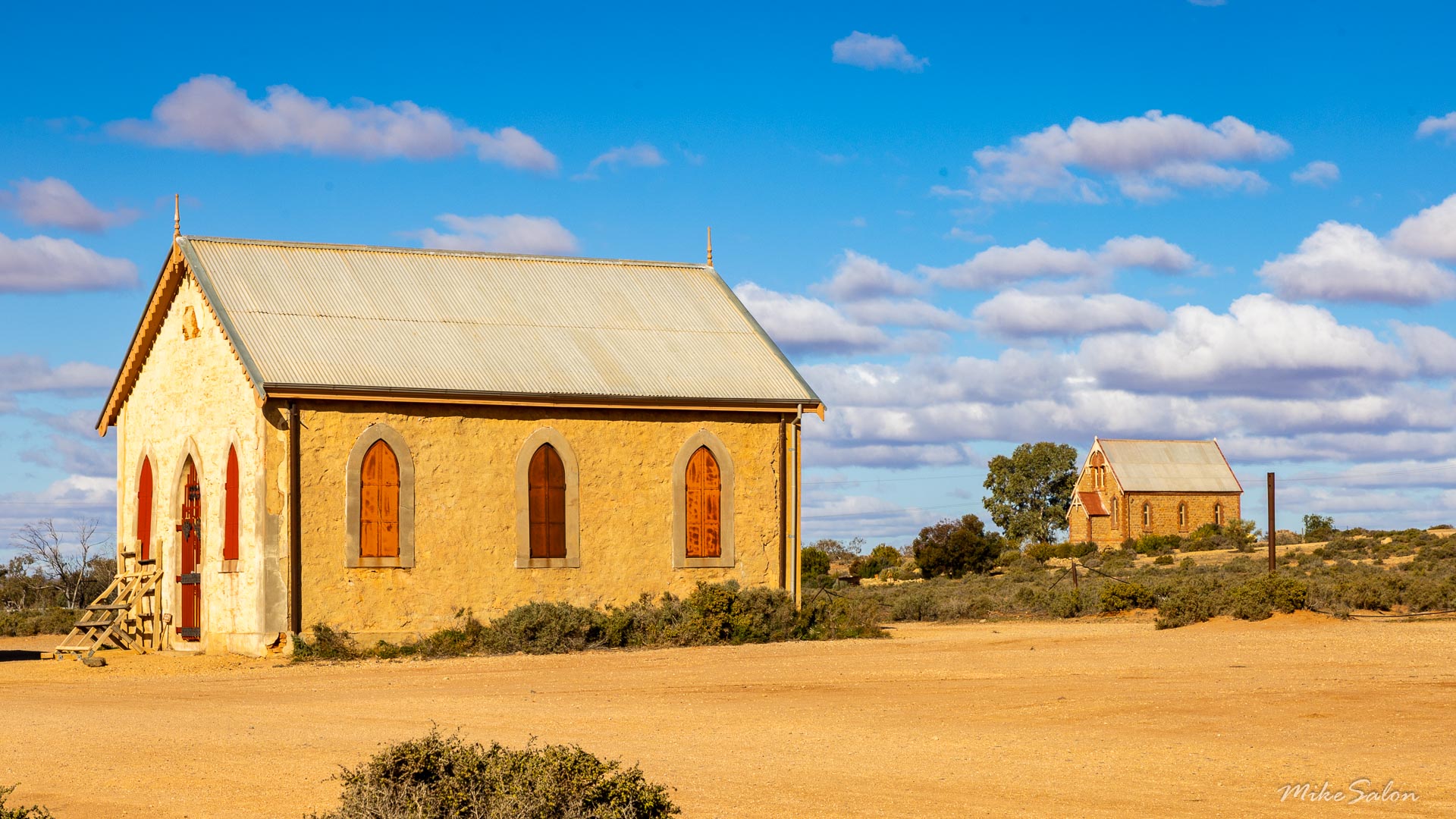 Small stone church with arched windows and pitched roof in open desert landscape.