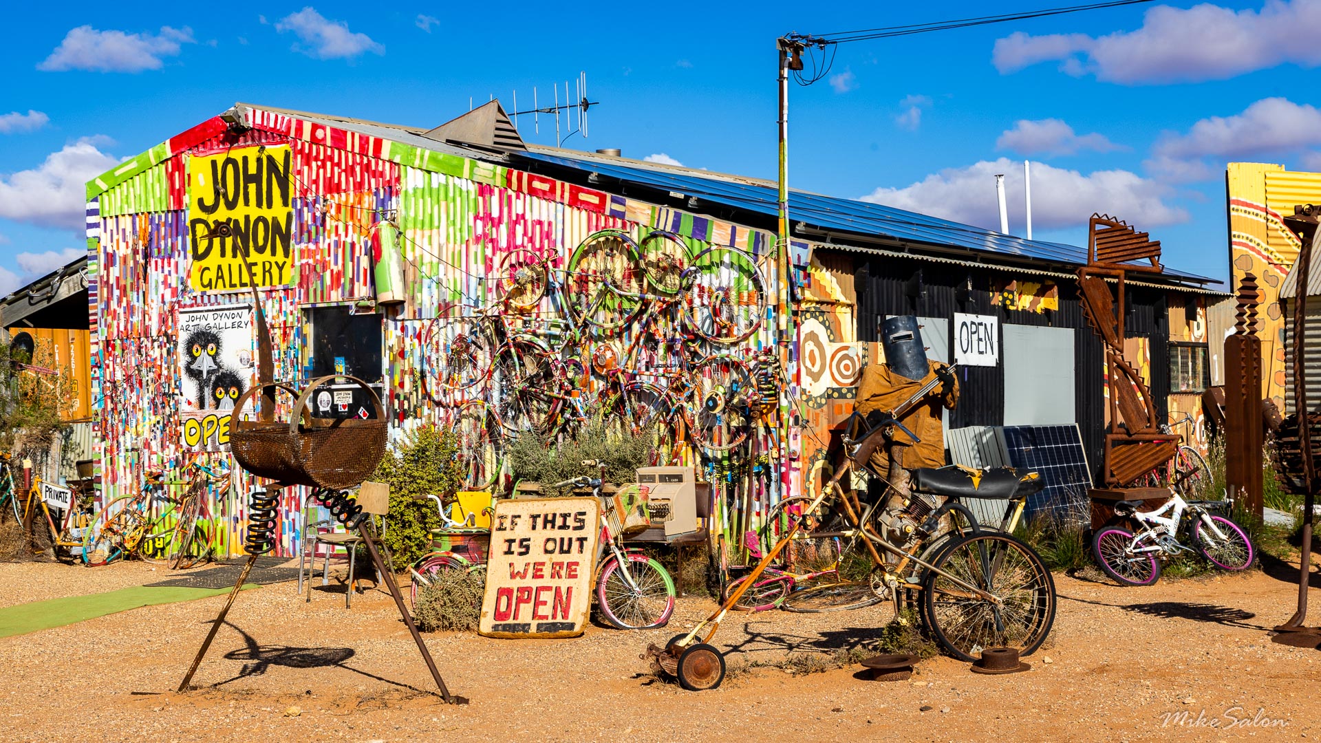 Brightly painted gallery building with graffiti‑style artwork, bicycle sculptures, and sign "John Dynon Gallery."