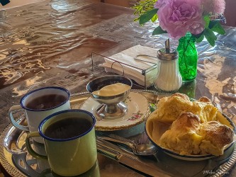  Table with teapot, cups, pastries, and small vase with flower in rustic setting.