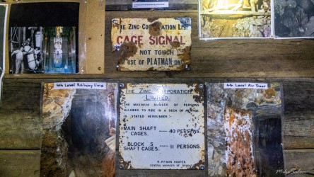 Wooden wall with old metal signs and photos, including "Cage Signal" and "Maximum Load 4 Persons."