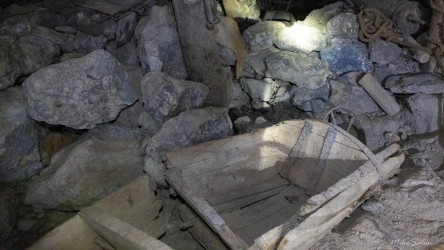 Underground scene showing wooden mining cart among rocks lit by headlamp.