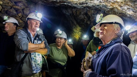 Group of people wearing helmets with headlamps inside mine tunnel listening to guide.
