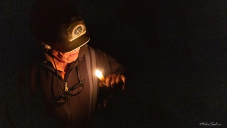 Person holding candle in dark underground space, face softly illuminated.