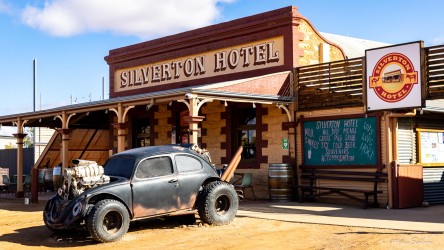 Historic Silverton Hotel with veranda, signage, and vintage black car parked outside under blue sky.