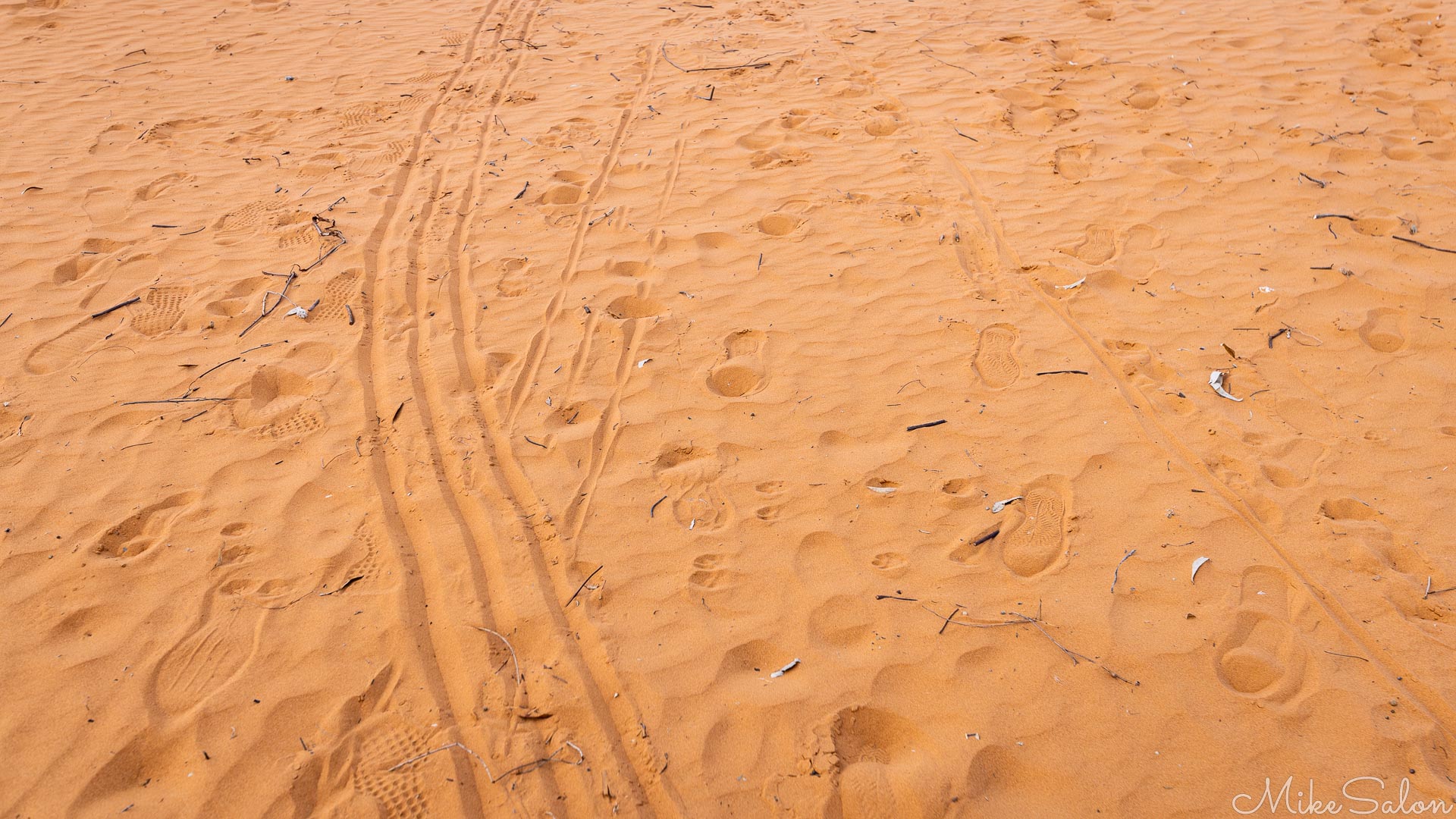 Close‑up of orange sand surface showing lines and footprints from tobogganing.