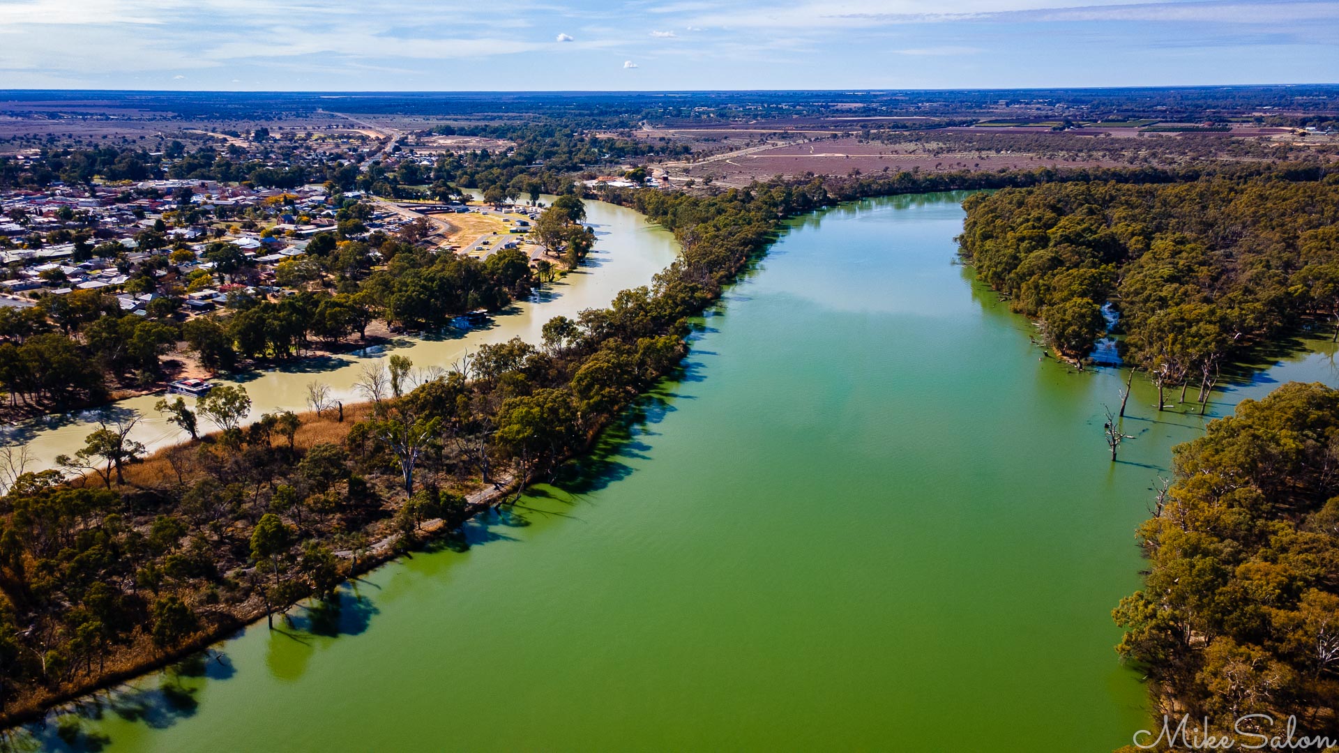 Aerial view of twin rivers running side by side through wooded landscape and town outskirts.