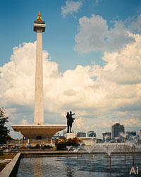 National Monument (Monas) with golden flame and Independence Statue beside fountain in central Jakarta under a bright sky.