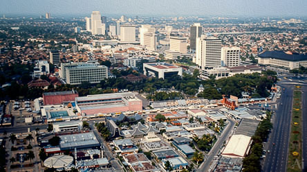 Aerial view of Jakarta showing mid‑century buildings, tree‑lined streets, and early high‑rises under hazy daylight.