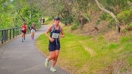 Bondi‑to‑Manly Ultra runners on a curving bushland path surrounded by trees and green slopes under soft daylight.