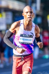 Elite marathon runner Victor Kipchirchir in white and purple kit running through Taylor Square during the Sydney Marathon 2025, focused and sweating under morning light.
