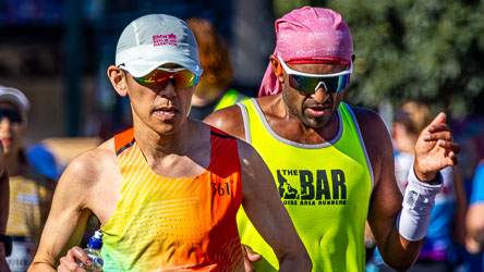 Two marathoners pass through Taylor Square at the 32 km mark — one wearing a “BMW Berlin Marathon” cap, the other representing “The BAR Boise Area Runners.” A fleeting moment of international camaraderie amid Sydney’s marathon rhythm. [3963]