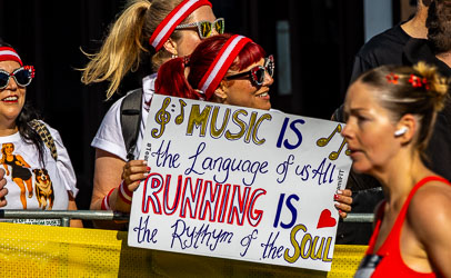 Spectators at Taylor Square cheer runners with a handmade sign reading “Music is the language of us all, running is the rhythm of the soul.” Their coordinated headbands and bright smiles capture the spirit of the Sydney Marathon’s most joyful corner. [3931]