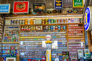 Interior of the Great Aussie Beer Shed showing shelves of vintage beer cans, Shell petrol pump, and old poker machines surrounded by colourful brewery signs.