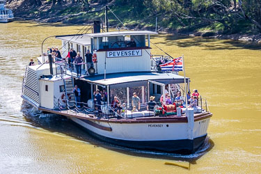 Historic paddle steamer P.S. Pevensey carrying passengers on the Murray River, flying the red‑white‑blue flag, approaching Echuca Wharf under sunny skies.