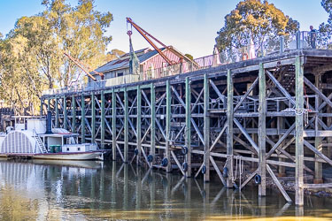 Reconstructed timber wharf at Port of Echuca with traditional riverboat moored alongside, showing the elevated wooden structure, lattice bracing and reflections in the Murray River.