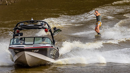 Person riding a board behind a motorboat on the Murray River, connected by a towline as the boat creates a large wake.