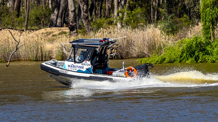 NSW Maritime patrol boat speeding along the Murray River, creating a wake near reeds and trees, marked with official signage and life ring.