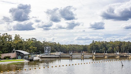View of Torrumbarry Weir on the Murray River showing the modern interpretive centre, weir gates, and surrounding river gums under a partly cloudy sky.