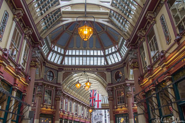 Interior of Leadenhall Market in London showing ornate Victorian architecture, glass roof, hanging lamps, and St George